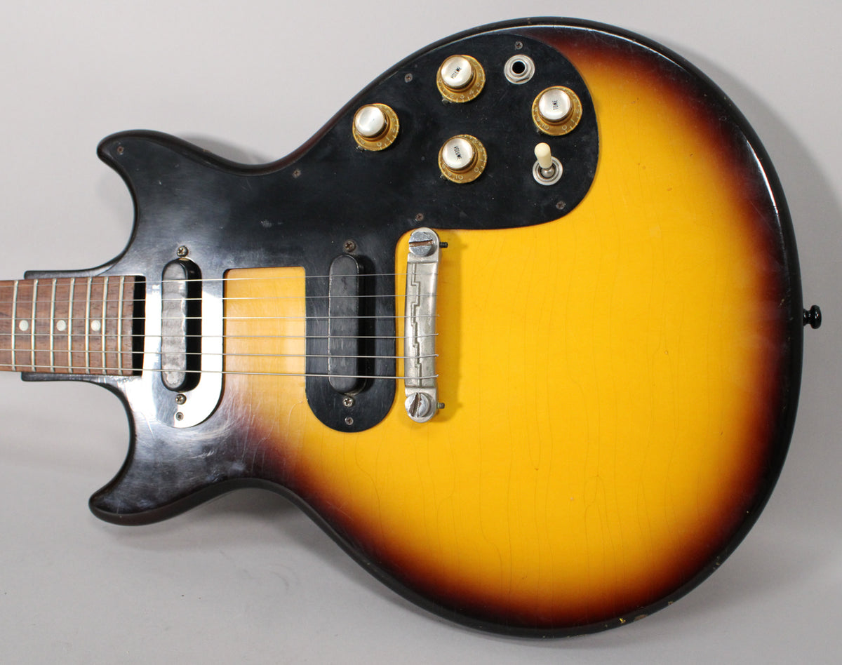 Close-up of the sunburst body, showing two black single-coil pickups, a chrome wraparound bridge, and four gold-capped control knobs.