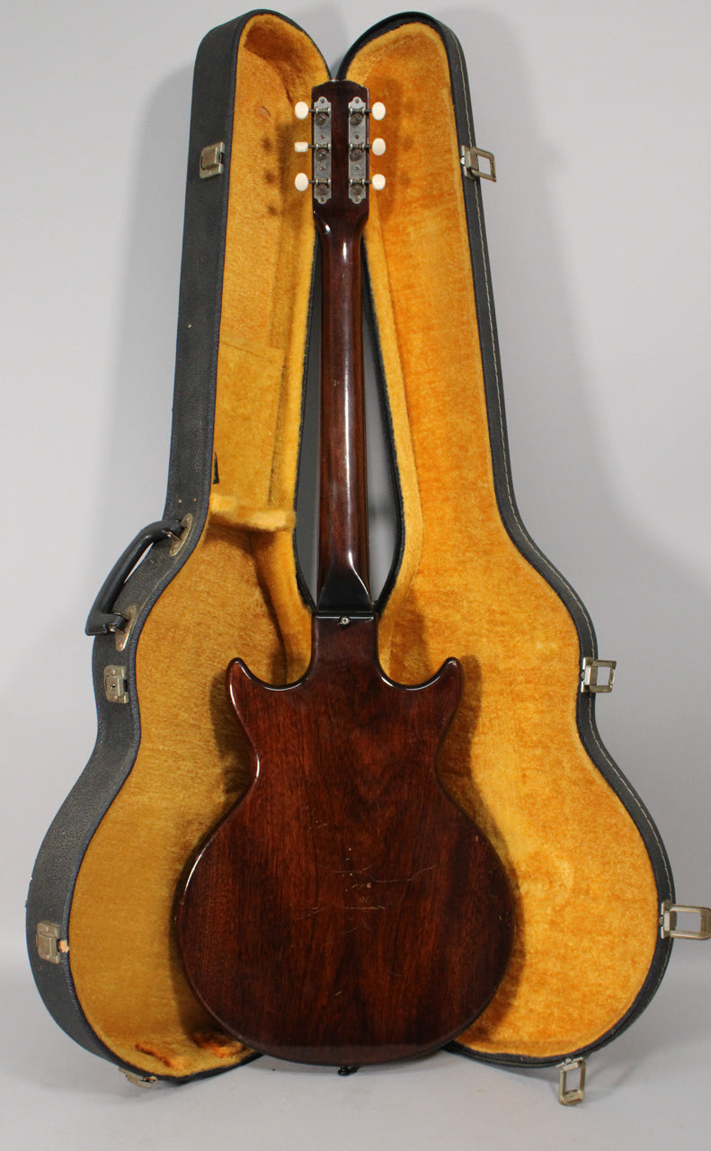 The guitar's dark sunburst back and neck are visible, with six white tuning pegs and a few scratches on the body.