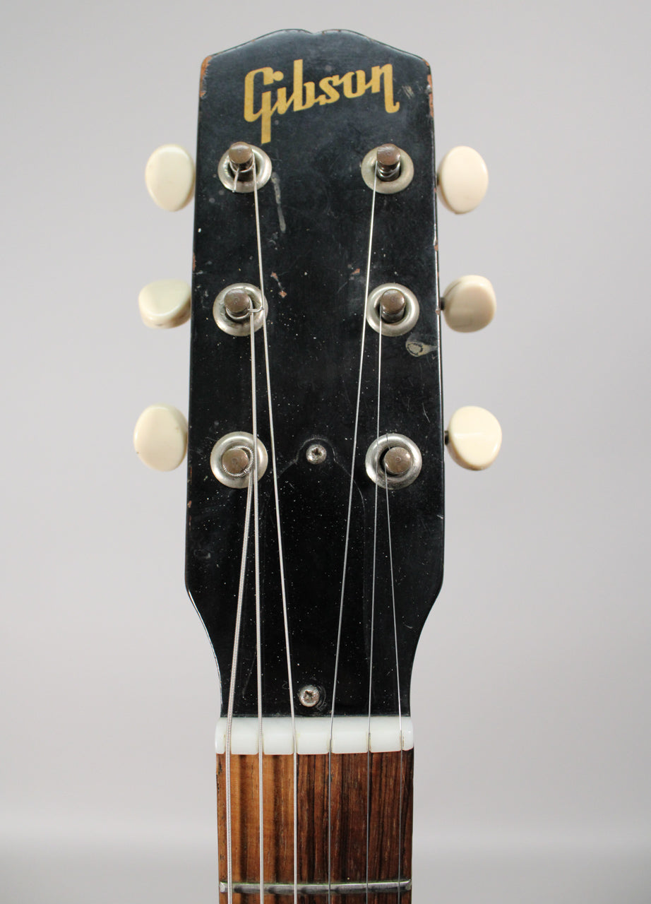 Close-up of the guitar's black headstock with six cream tuning pegs, showing wear, scratches, and a gold logo.