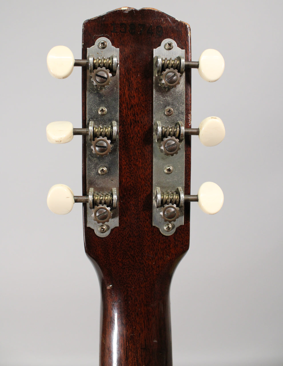 Rear view of the dark brown headstock and neck, showing six cream-colored tuning pegs on two metal strips with visible wear.