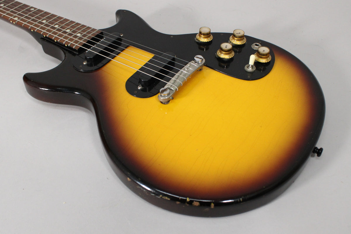 The sunburst guitar body, with a black pickguard, shows four gold knobs and a white switch, plus significant wear on the lower edge.