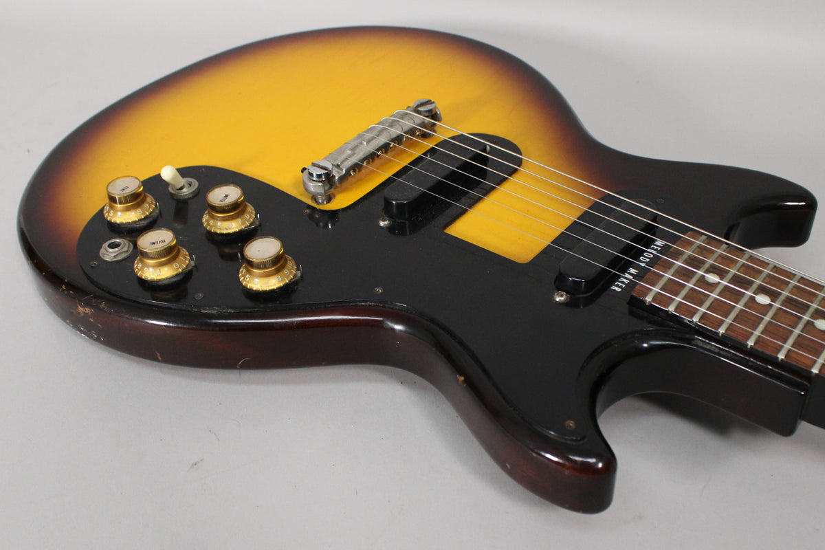 Close-up of the sunburst body, showing the black pickguard, four gold top hat knobs, a white switch, and two black single-coil pickups.