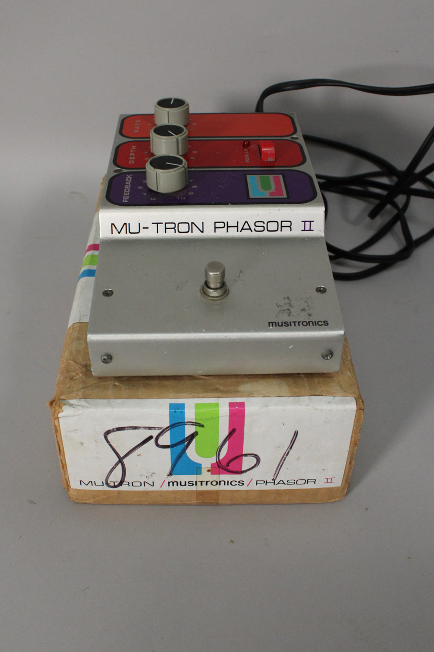 The silver pedal with three grey knobs, a red power switch, and a footswitch rests on its worn cardboard box.