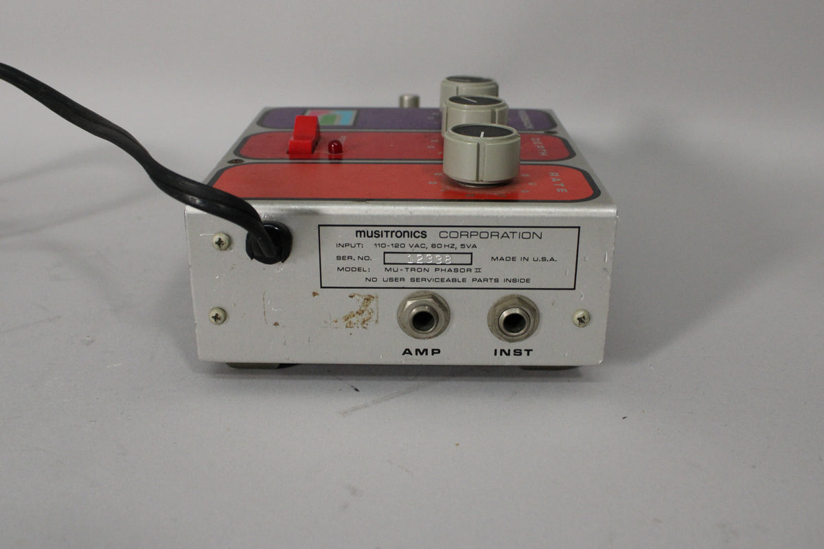 The silver pedal's rear panel is visible, showing two input jacks, a black power cable, and some scuffs on the metal casing.