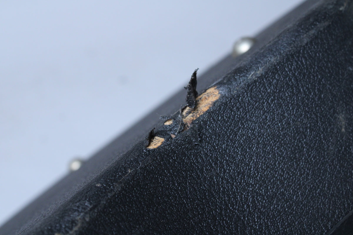 A close-up of the black textured case shows a large tear in the covering, revealing the lighter wood underneath.