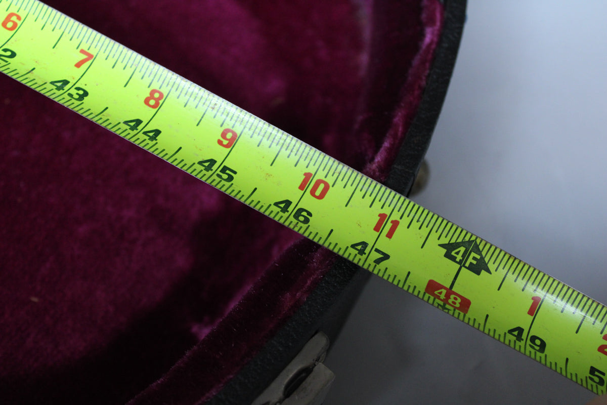 A bright yellow tape measure extends diagonally across the open case, showing the deep purple plush interior.