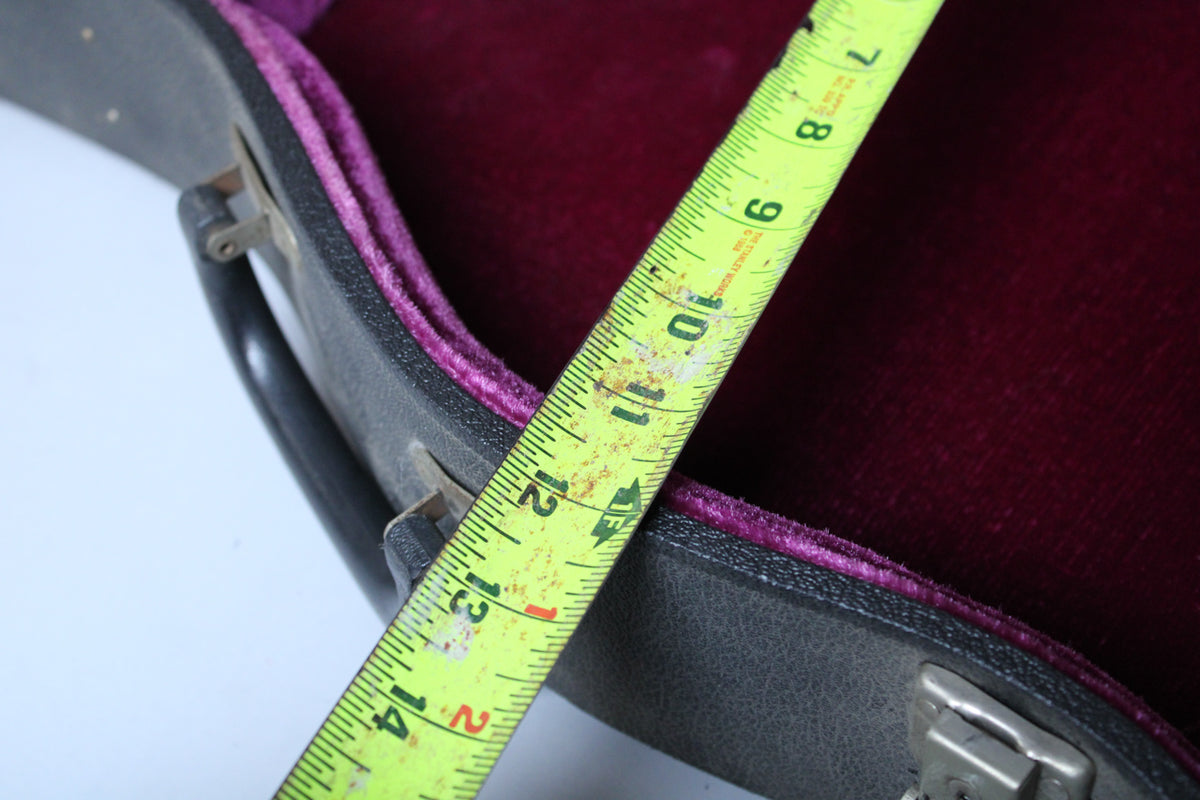 A yellow tape measure spans the open, dark grey case with a deep red velvet interior, showing wear and dust.