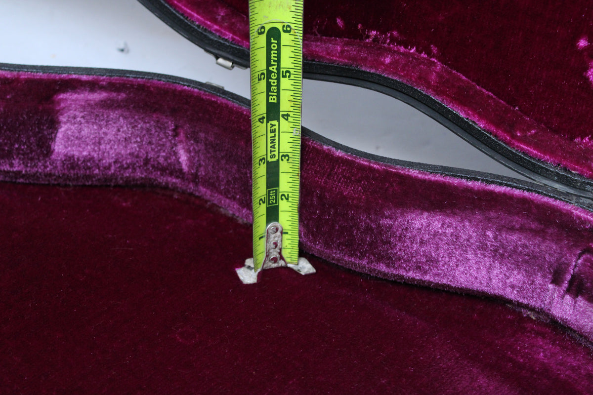 Close-up of the case's deep purple plush interior, with a tape measure showing the depth of the guitar body cavity.