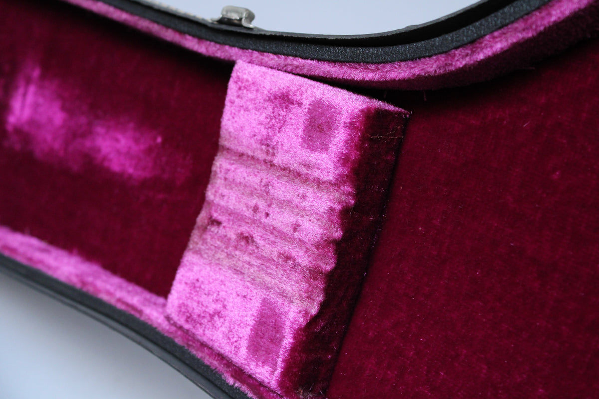 Close-up of the case's interior, showing the dark red plush lining and a lighter pink, worn velvet support block.