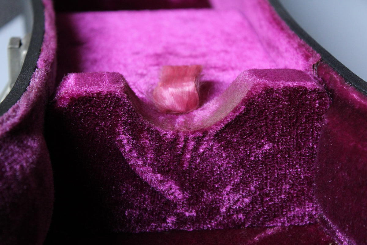 Close-up of the case's interior, showing the vibrant magenta plush lining with a neck support and a small pink ribbon.