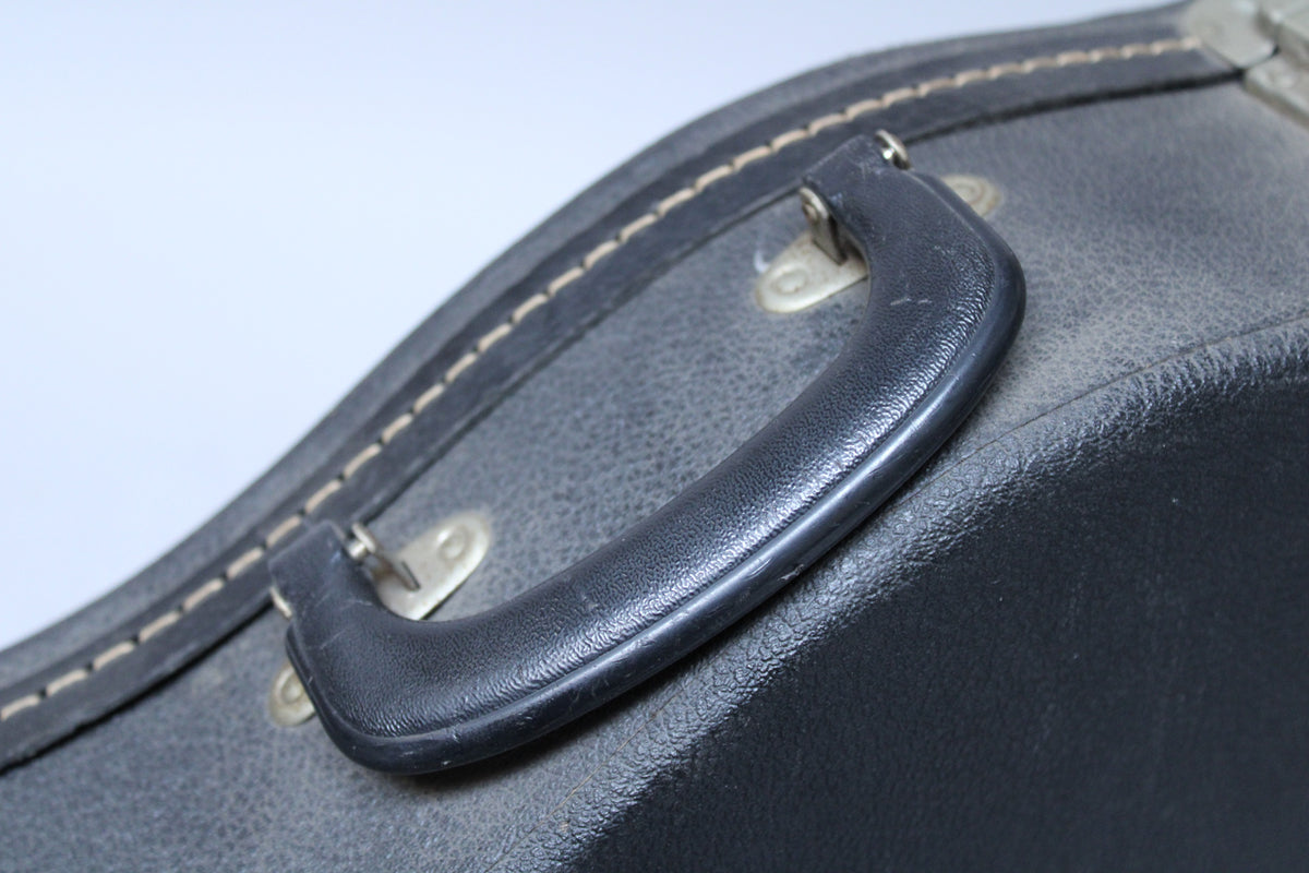 Close-up of the black textured case handle and surrounding worn black tolex, with visible light-colored stitching along the case edge.