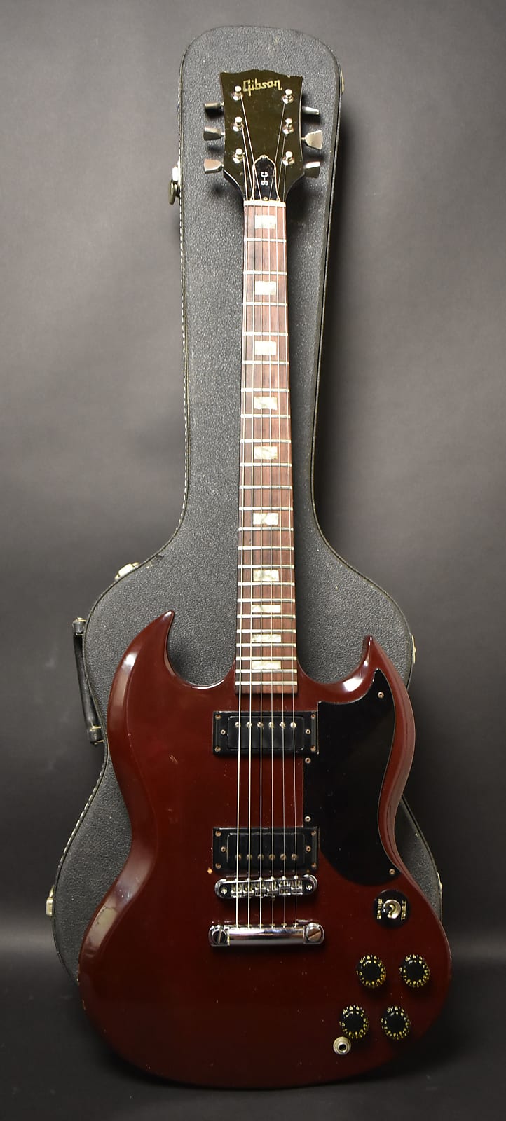 A cherry red Gibson SG Special with a black pickguard and four control knobs rests in a black hard shell case.