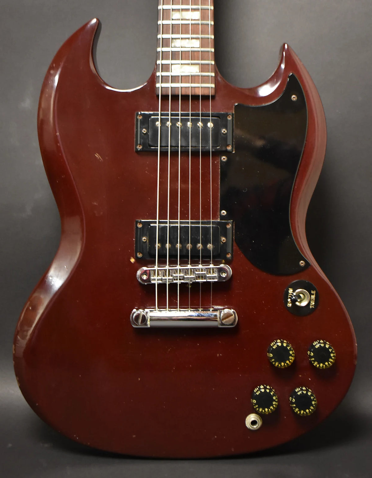 Full-frame view of a cherry red SG with a black pickguard, two humbuckers, a tune-o-matic bridge, and four black-and-gold knobs.