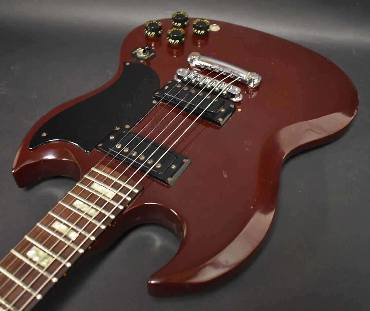 Cherry red SG body, angled from the lower bout, showing black pickguard, two humbuckers, chrome bridge, and four black control knobs.