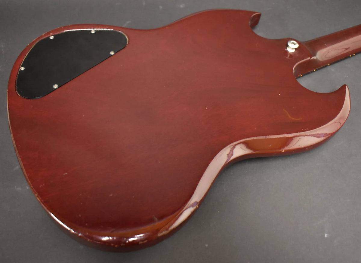 The back of a cherry red guitar body, showing a black control cavity cover and significant finish wear along the edges.