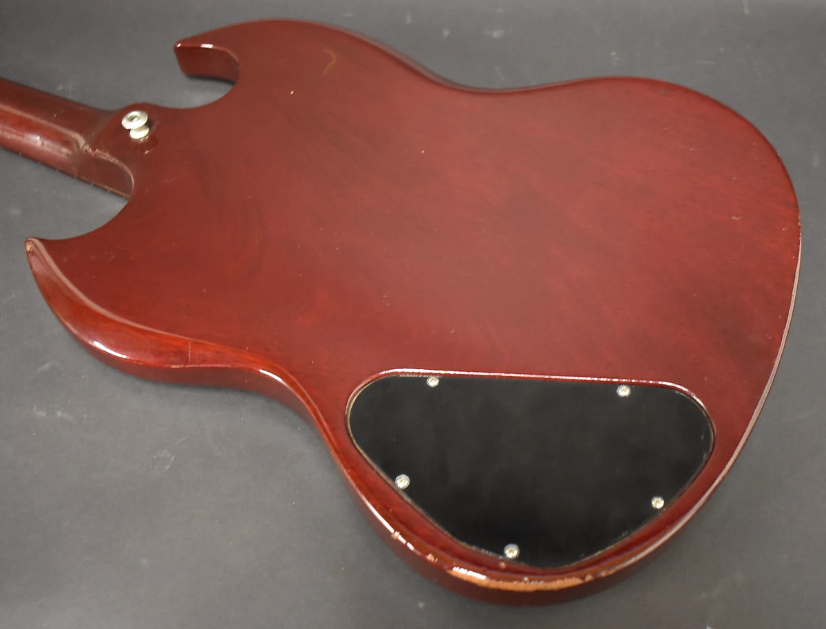 The cherry red guitar's back shows a black control cavity cover, a strap button, and wear along the lower body edge.