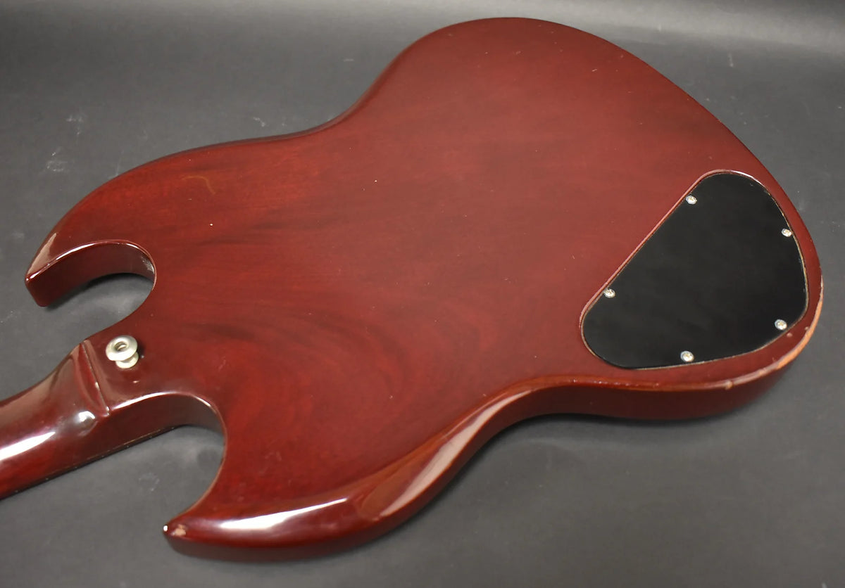 The cherry red SG's back shows a black control cavity cover, a strap button, and notable finish wear along the lower edge.