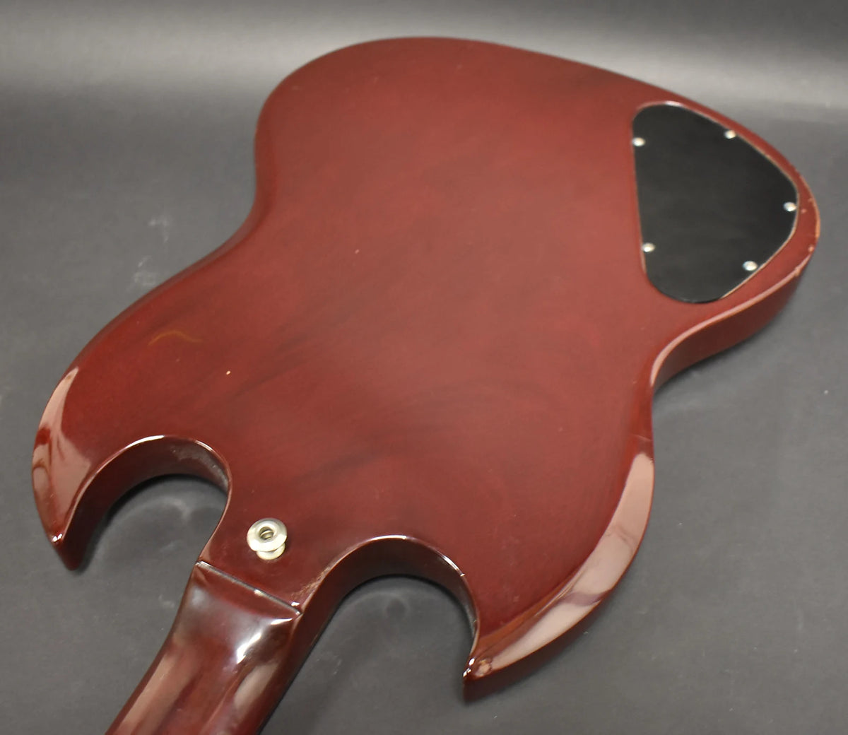 The back of the cherry red SG body, showing the neck joint, black control cavity cover, and some finish wear.