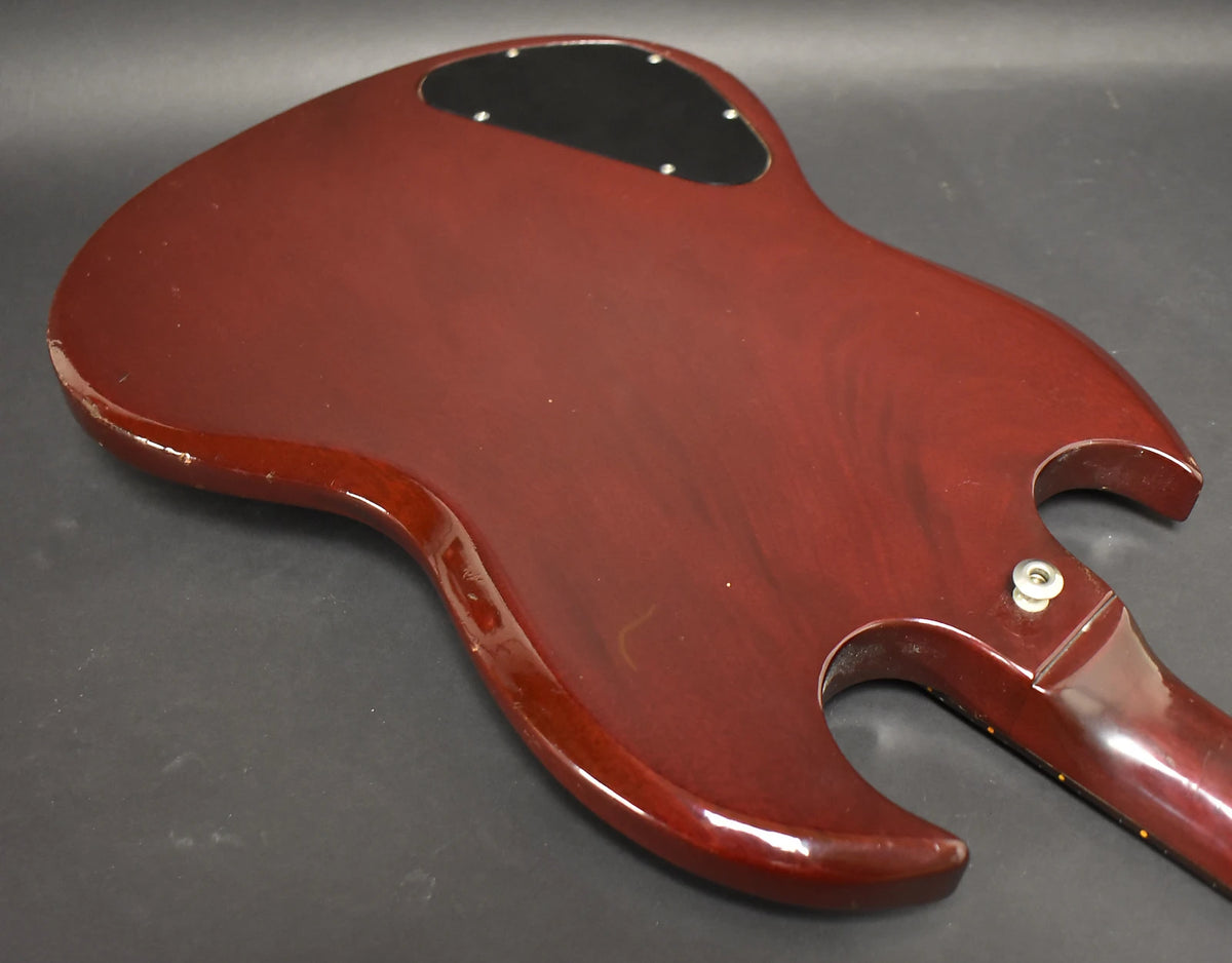 The back of a cherry red SG, showing a black control cavity cover, strap button, and visible wear along the edges.