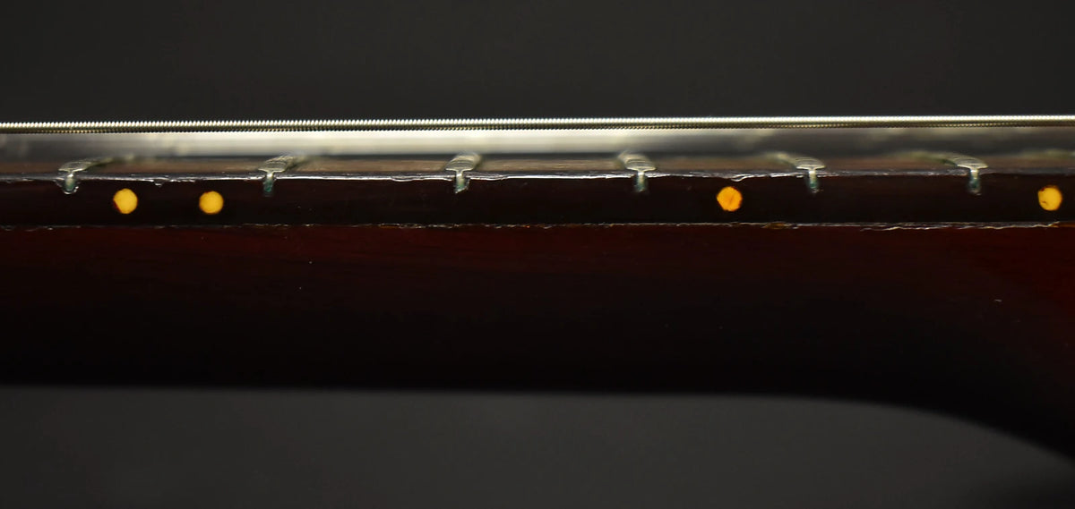 Close-up of the guitar's dark brown fretboard from the side, showing five frets, four round yellow dot inlays, and strings.