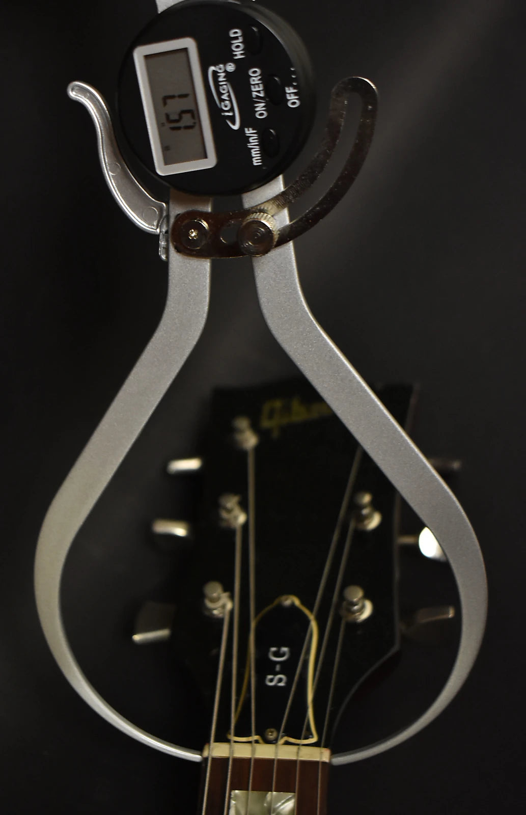 Close-up of the guitar's headstock, with a digital caliper measuring 1.57mm across the nut, showing some light wear.