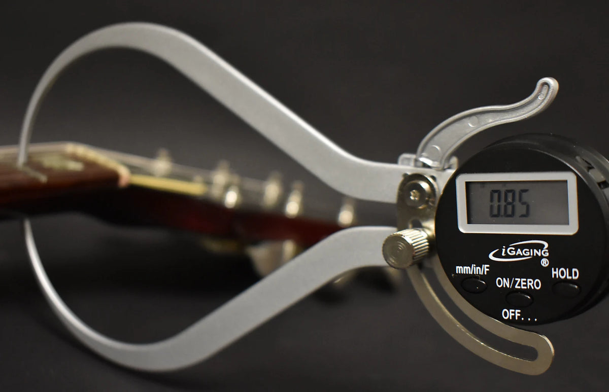 A digital caliper measures the guitar's neck thickness at the first fret, showing 0.85 inches.