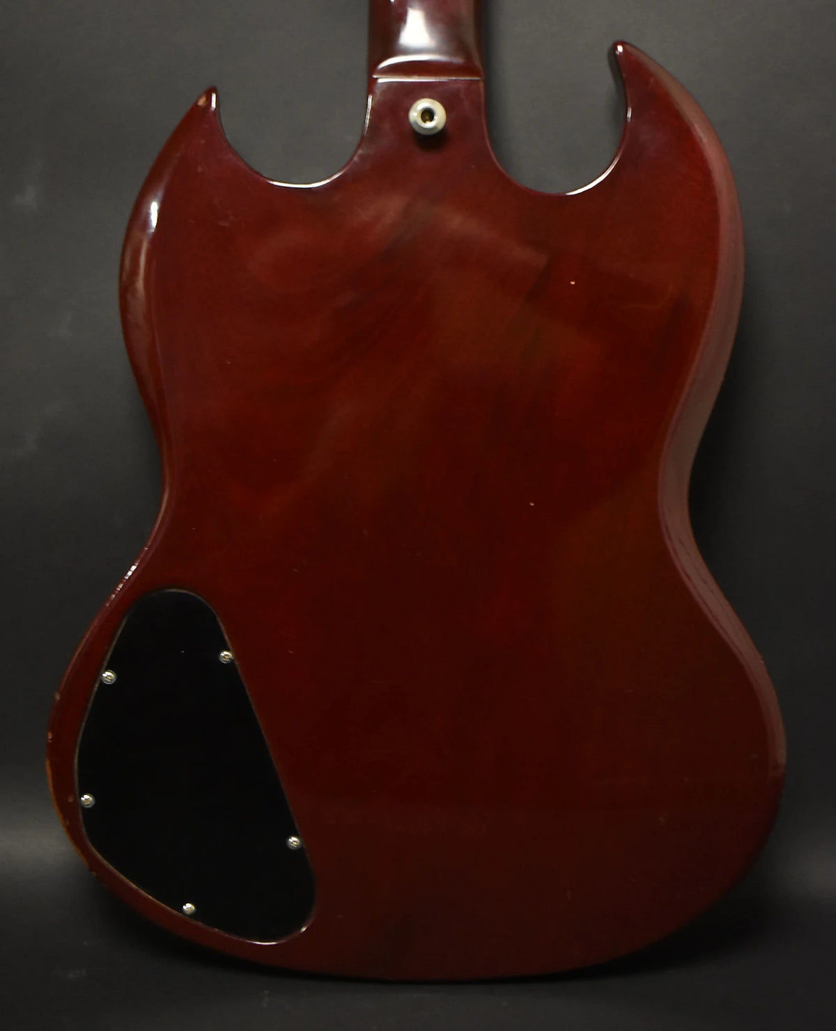Rear view of a cherry red SG guitar body with a black control cavity cover and a strap button at the neck heel.