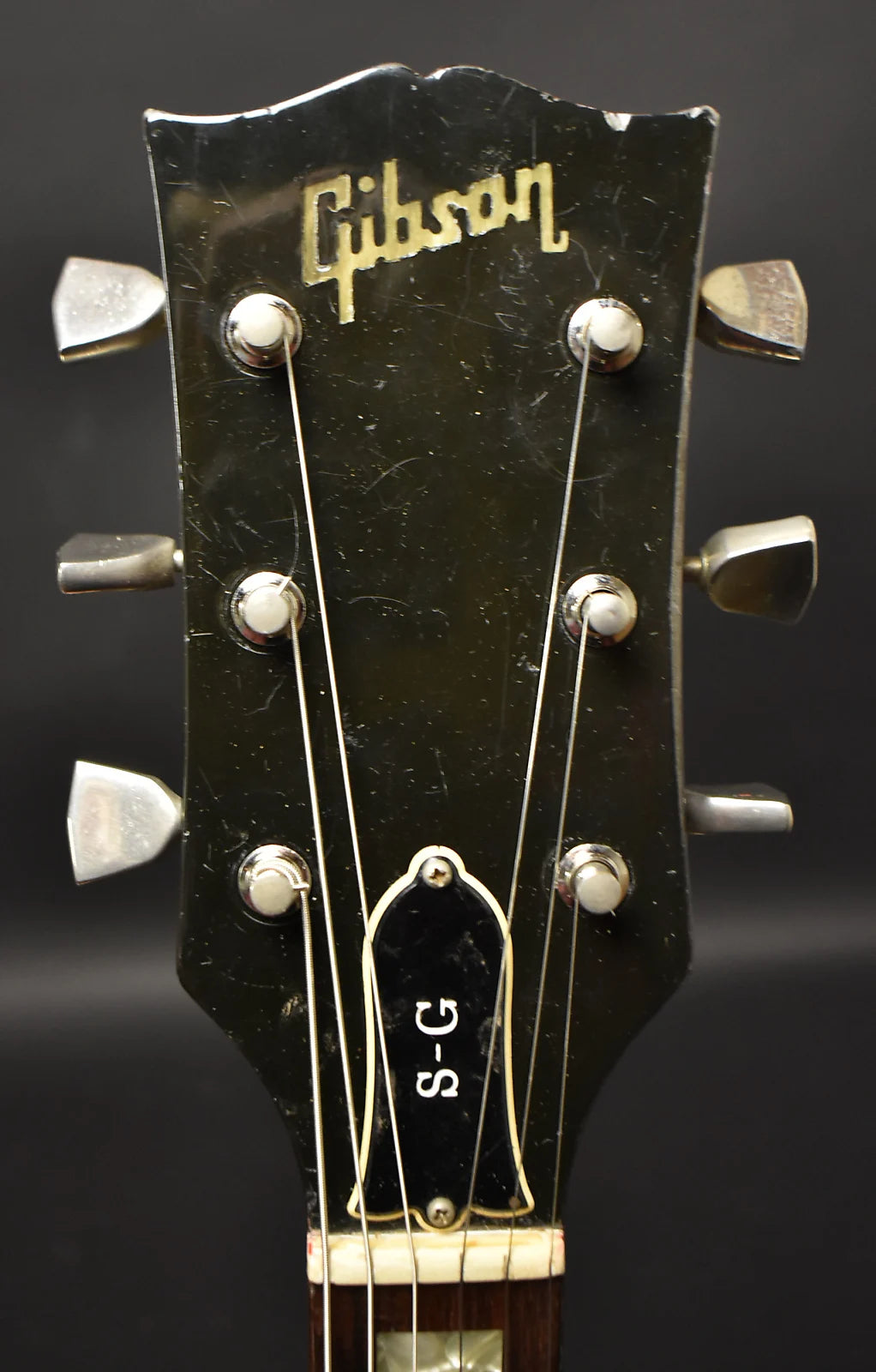 Close-up of the black headstock with gold Gibson logo, showing six chrome tuners, a black truss rod cover, and heavy finish wear.