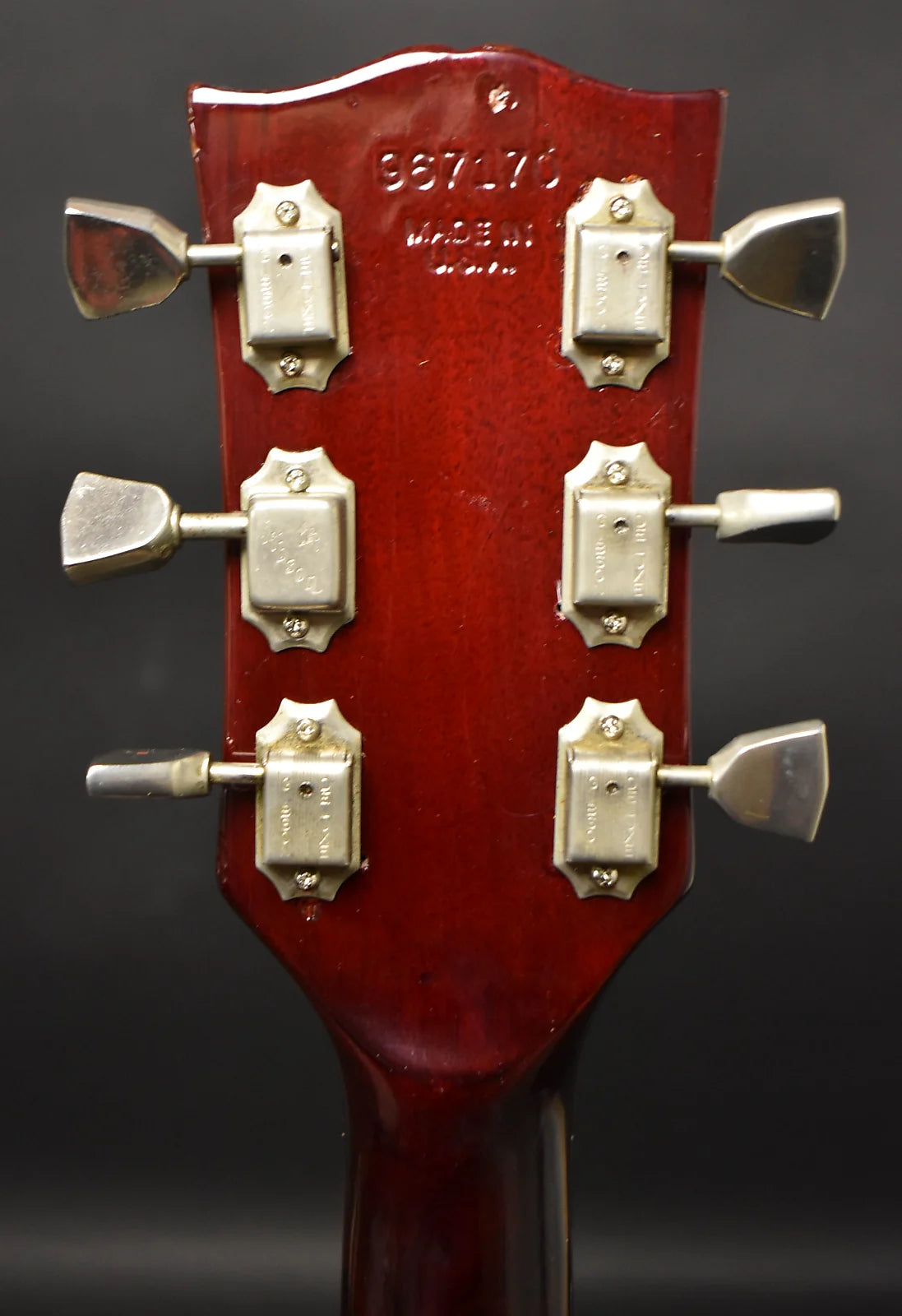 Rear view of the cherry red headstock with six chrome tuners, showing finish wear and a serial number stamped into the wood.