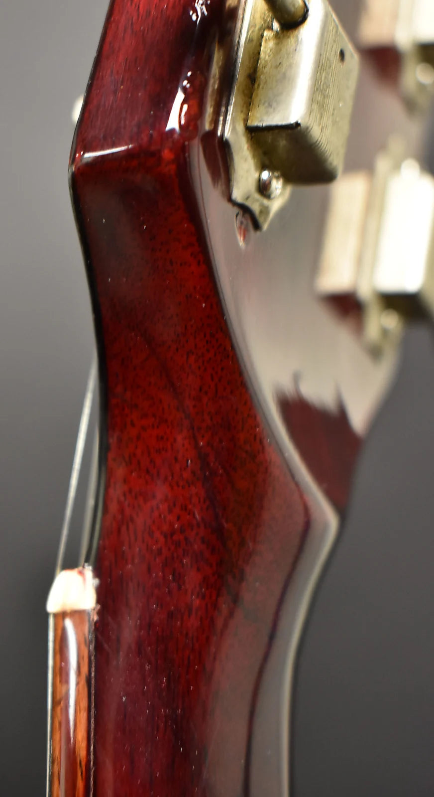 Close-up of the cherry red guitar headstock, showing a worn, tarnished tuning machine and light finish checking.