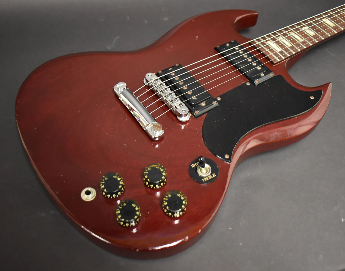 Close-up of a cherry red Gibson SG Special's body, showing the bridge, pickups, black pickguard, four control knobs, and toggle switch.