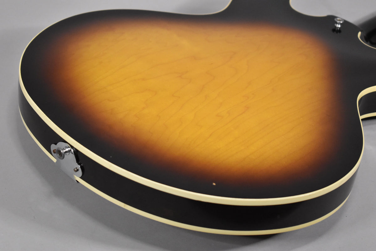 The guitar's sunburst back, with a visible wood grain, shows a small ding near the lower bout and a chrome output jack plate.