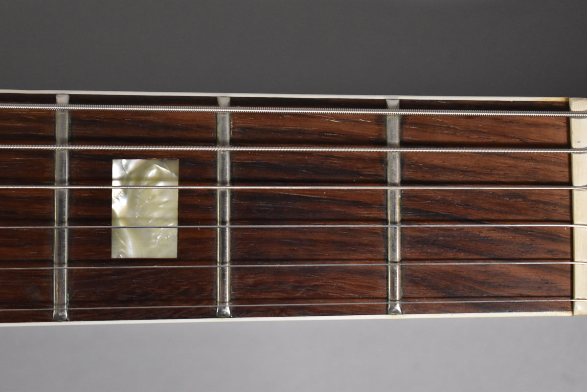 Close-up of the dark rosewood fretboard with rectangular mother-of-pearl inlay at the 7th fret, showing light wear on the frets.