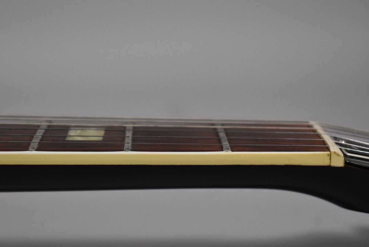 Close-up of the guitar's dark fretboard and frets, with a single rectangular pearloid inlay visible, and cream binding along the edge.