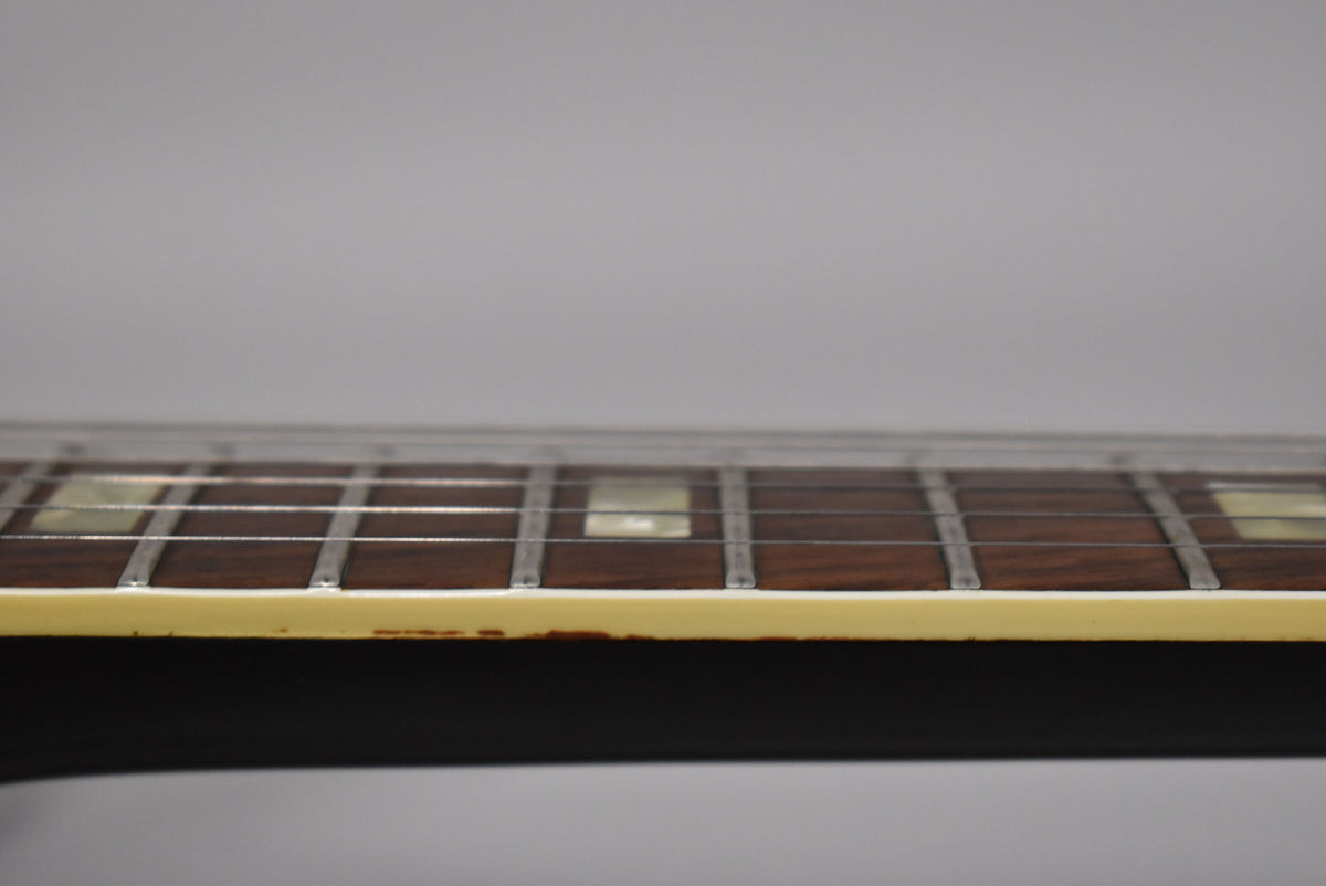 Close-up of the guitar's dark fretboard and frets, showing rectangular inlays and wear along the cream binding on the lower edge.