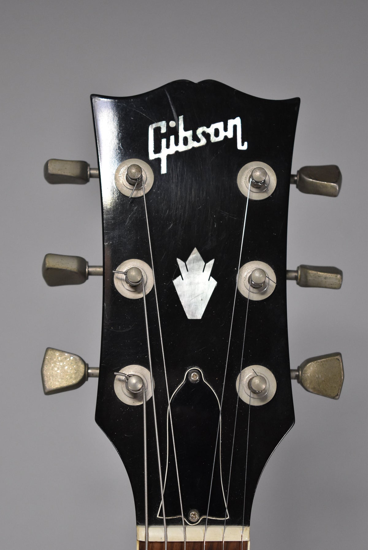 Close-up of the black headstock with mother-of-pearl inlay, six tarnished metal tuners, and visible wear and light scratches.