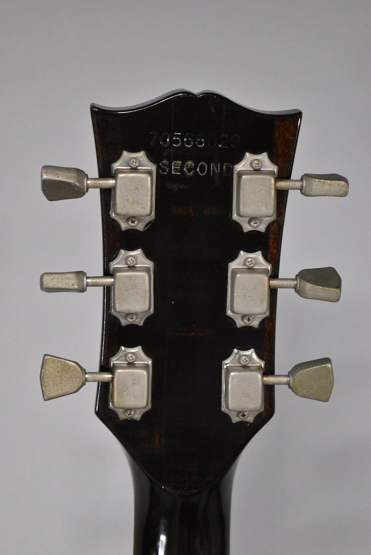Rear view of the dark brown headstock, showing six trapezoid-button tuners with tarnished nickel plating and visible wear.