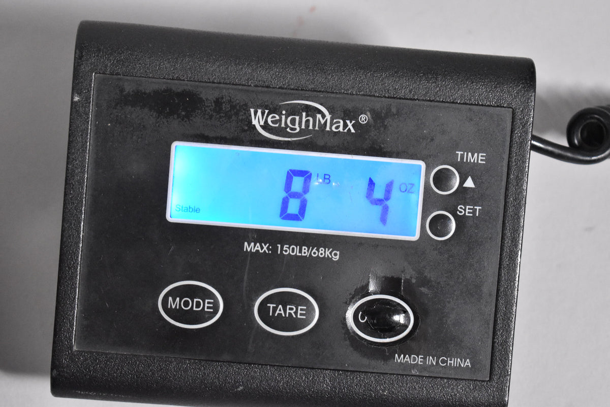 A close-up of a black digital scale displaying "8 LB. 4 OZ." in blue, with "WeighMax" and "MADE IN CHINA" visible.