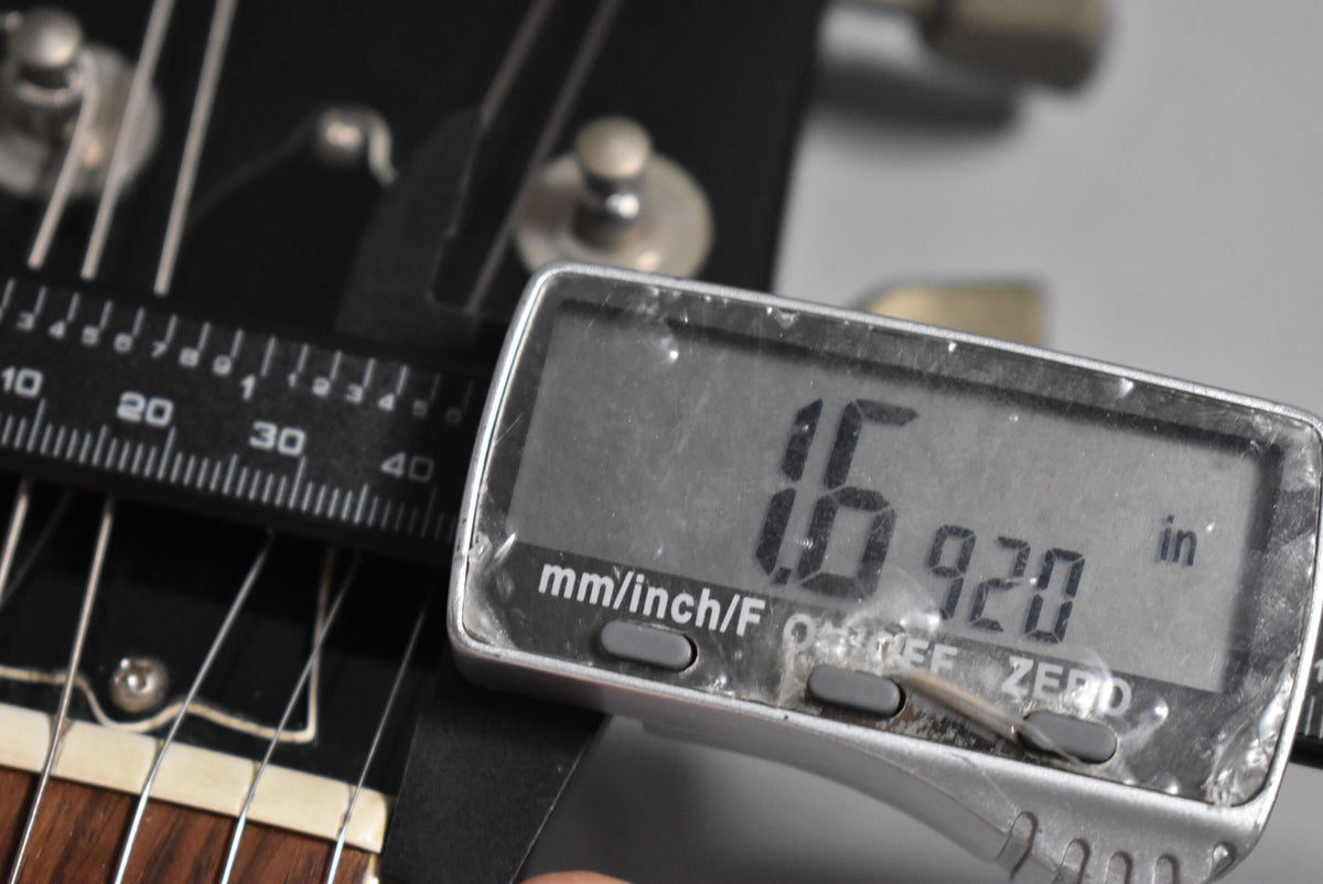 A digital caliper measures the nut width of the guitar at 1.6920 inches, with the headstock and tuning pegs visible.