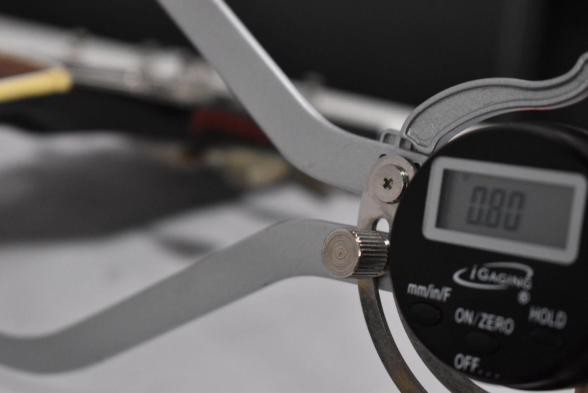 A close-up of a digital caliper with a reading of 0.00, with blurred background elements.