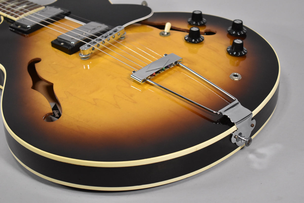 Close-up of the sunburst body, showing the f-hole, chrome trapeze tailpiece, bridge, two humbuckers, and four black control knobs.