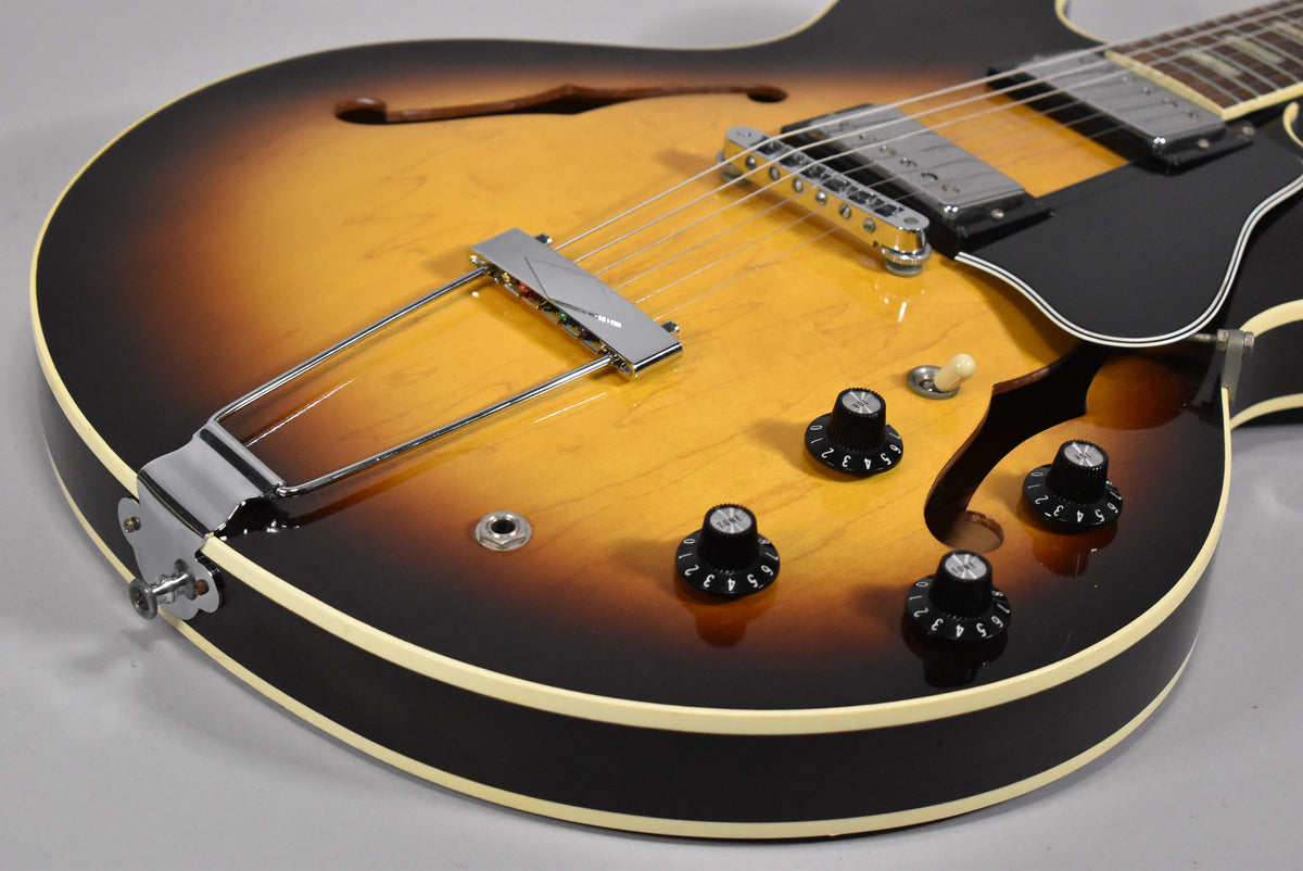 Close-up of the sunburst body, showing the chrome trapeze tailpiece, bridge, neck pickup, black pickguard, and four black control knobs.