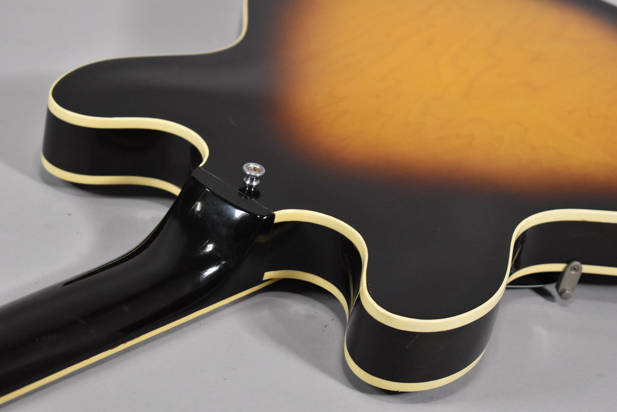 The guitar's sunburst body and neck heel are visible, with cream binding and a strap button on the upper horn.
