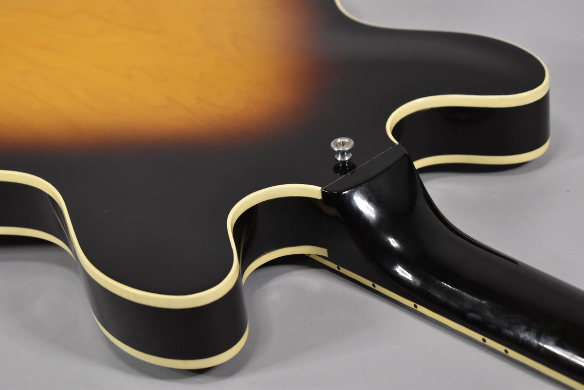 Upper body and neck joint of a sunburst guitar, showing the black lower bout, cream binding, and a strap button.