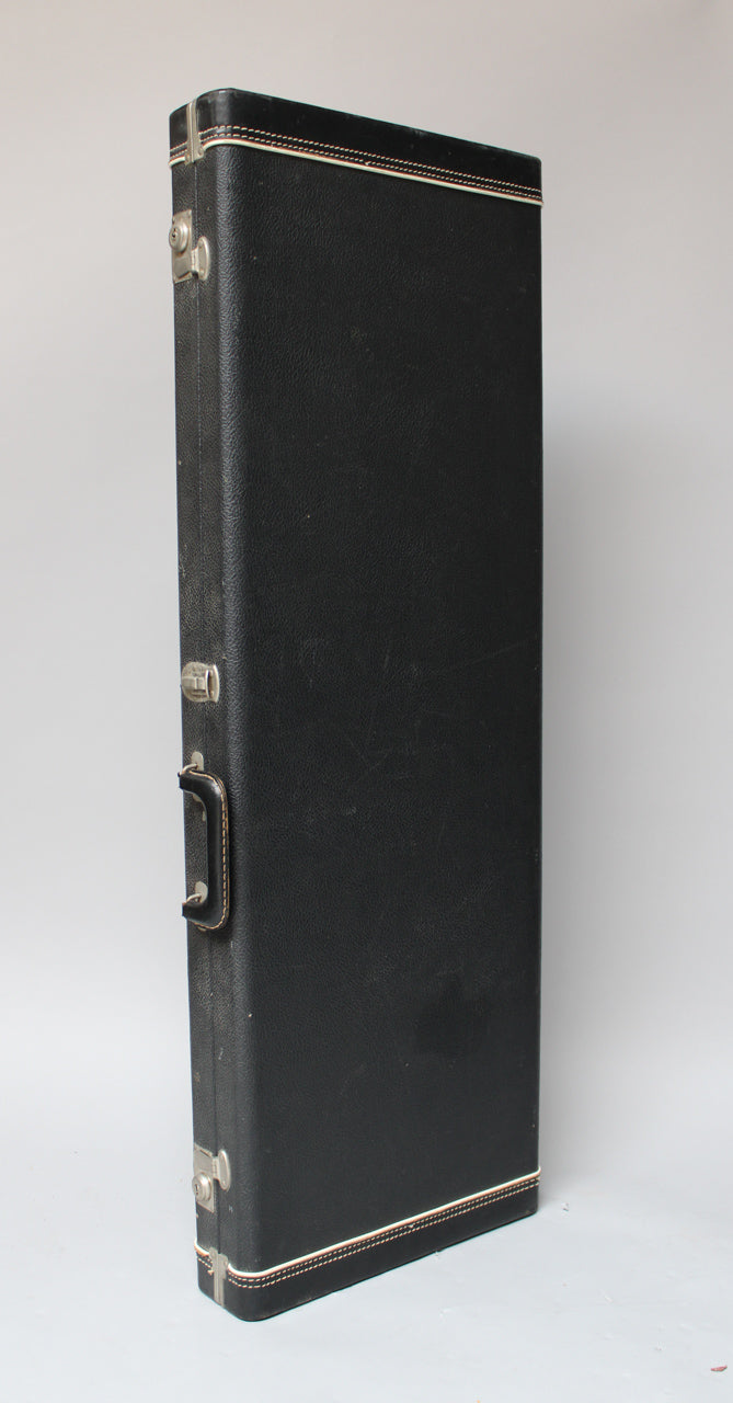 Black textured hard case, standing upright, showing the side with a handle, three latches, and white piping with red stitching.