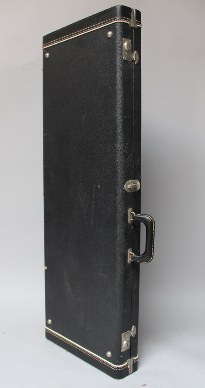 Black textured hard case, viewed from the side, showing the handle, three latches, and white piping along the edges.
