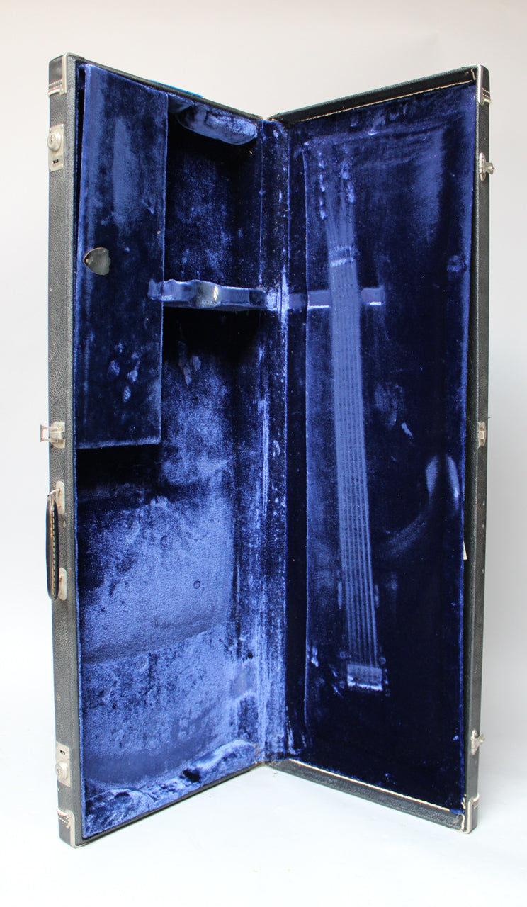 Open black hard case with a worn blue velvet interior, showing a storage compartment and neck support.