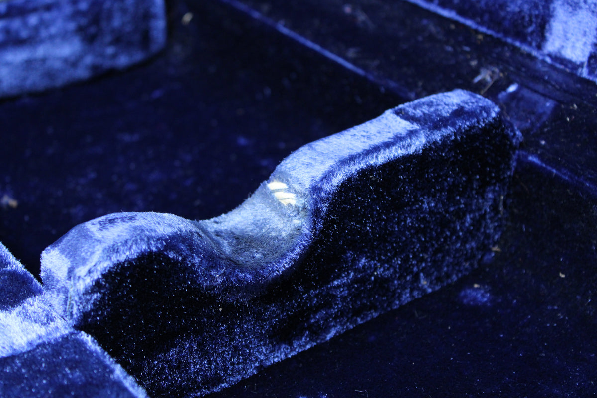 Close-up of the case's dark blue plush interior, showing a worn, curved support with a small tear revealing white material.