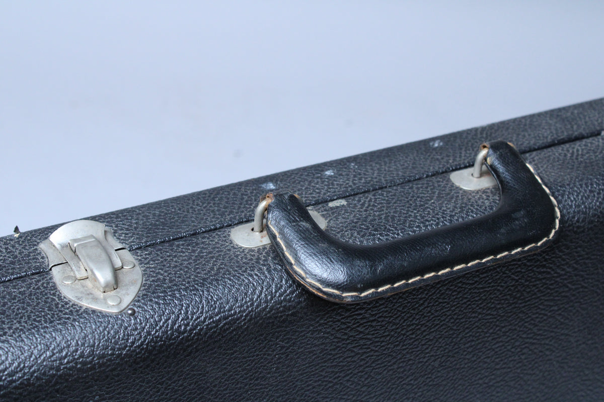 A close-up of the black textured case shows a silver latch and a black handle with white stitching, both with visible wear.