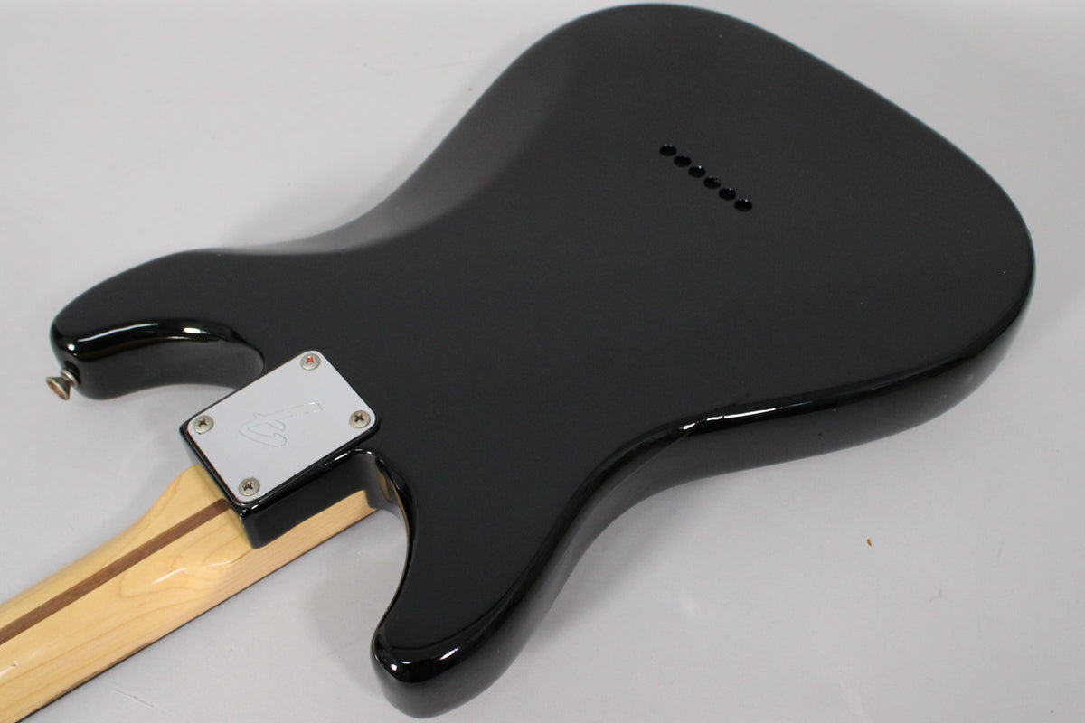 The black guitar body, viewed from the back, shows a shiny finish, a silver neck plate, and six string-through-body holes.